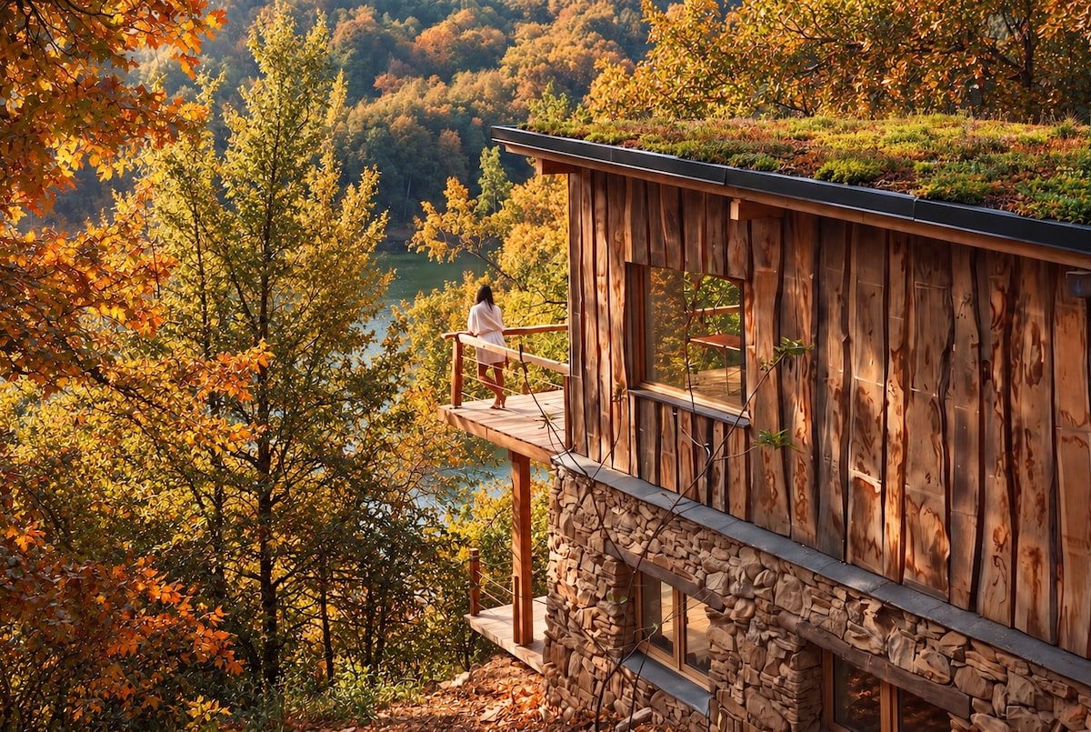 A wooden cabin with a stone foundation, a balcony, and a view of a forested valley.