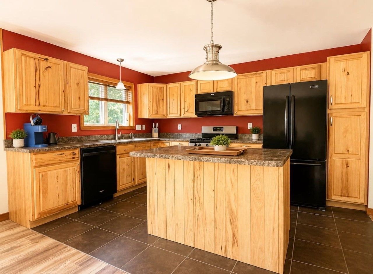 A kitchen with wooden cabinets, a central island, a black refrigerator, and a microwave.