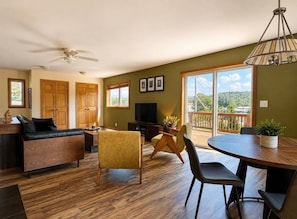A modern living room with a sofa, chairs, a dining table, a TV, and a balcony with a view. - 5th Street Trail House- 3Bed- 2Bath (Davis)