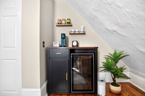 Eine kleine Küche mit einem Kühlschrank, einer Kaffeemaschine und einem Regal mit Gläsern.