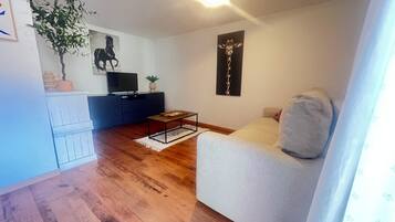 A living room with a sofa, a coffee table, a TV on a stand, a plant, and a wall art piece.