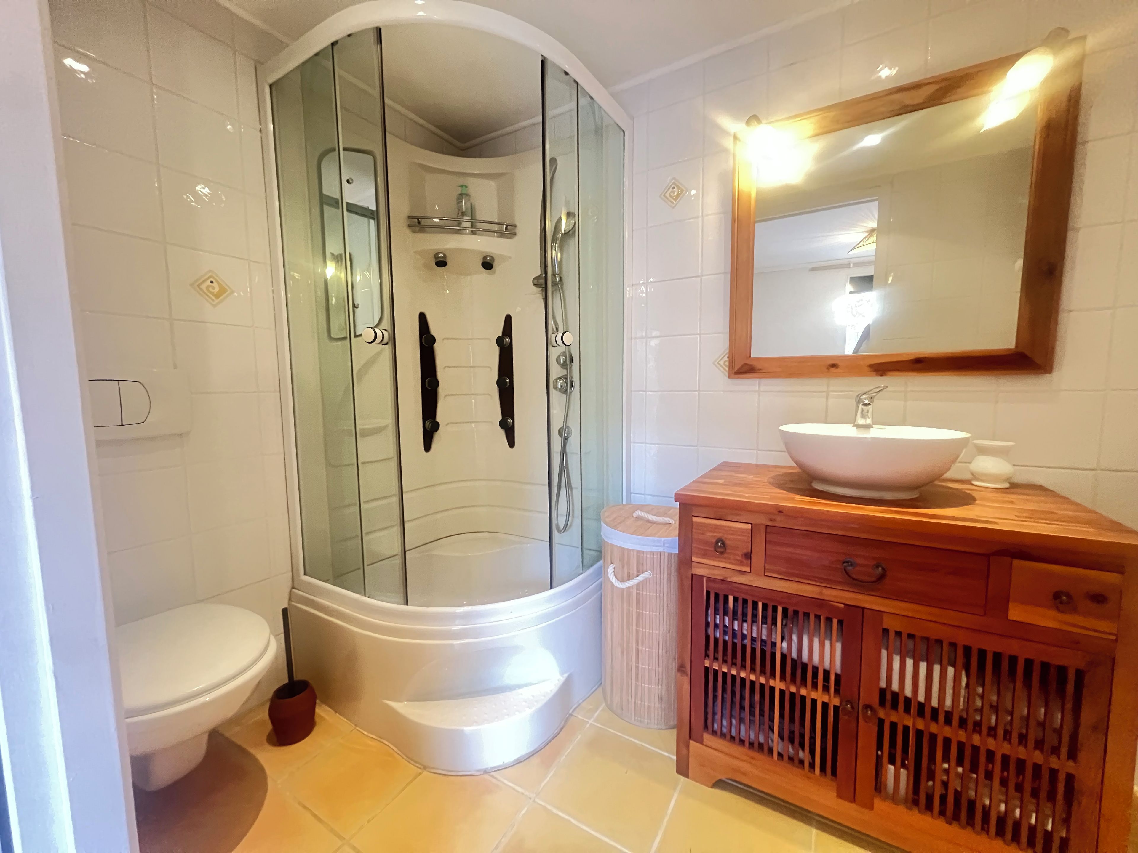 Ein Badezimmer mit einer gläsernen Duschkabine, einem weißen Waschbecken und einem Holzbadezimmer.