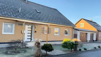 En bostadsbyggnad med en fasad av tegel, ett tak täckt med takpannor och en liten trädgård framför huset med olika buskar och ett träd.