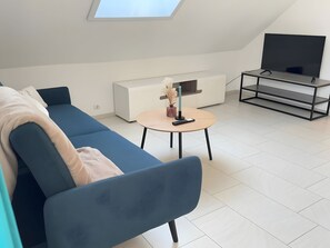 Ett modernt vardagsrum med en blå soffa, ett litet runt bord, en tv på ett tv-bord och ett takfönster.