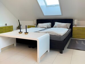 Ein modernes Schlafzimmer mit Dachfenster, einem Bett mit zwei Kissen, einem Nachttisch und einem Schreibtisch.