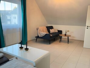 Ein moderner, hell erleuchteter Raum mit einem Bett, einem Sofa, einem kleinen Tisch und einem Fenster mit Vorhängen.