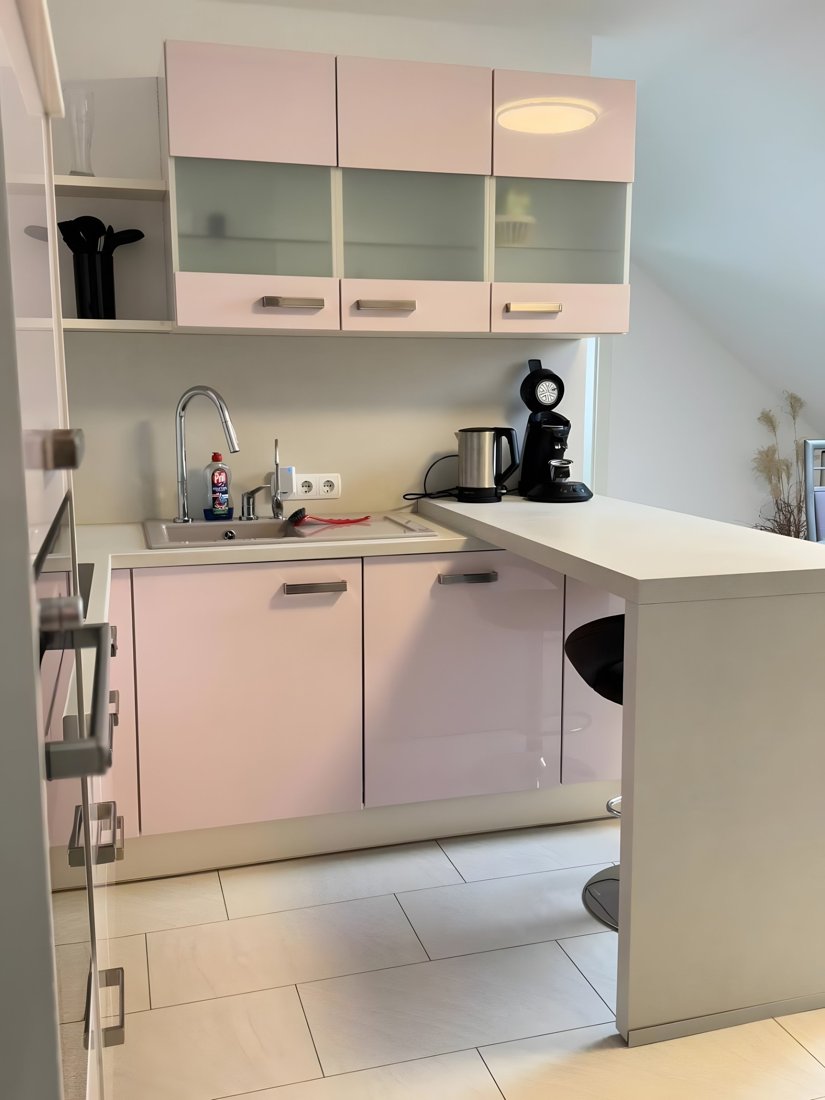 Eine moderne Küche mit weißer Arbeitsplatte, einem Spülbecken, einer Kaffeemaschine und einem Wasserkocher.