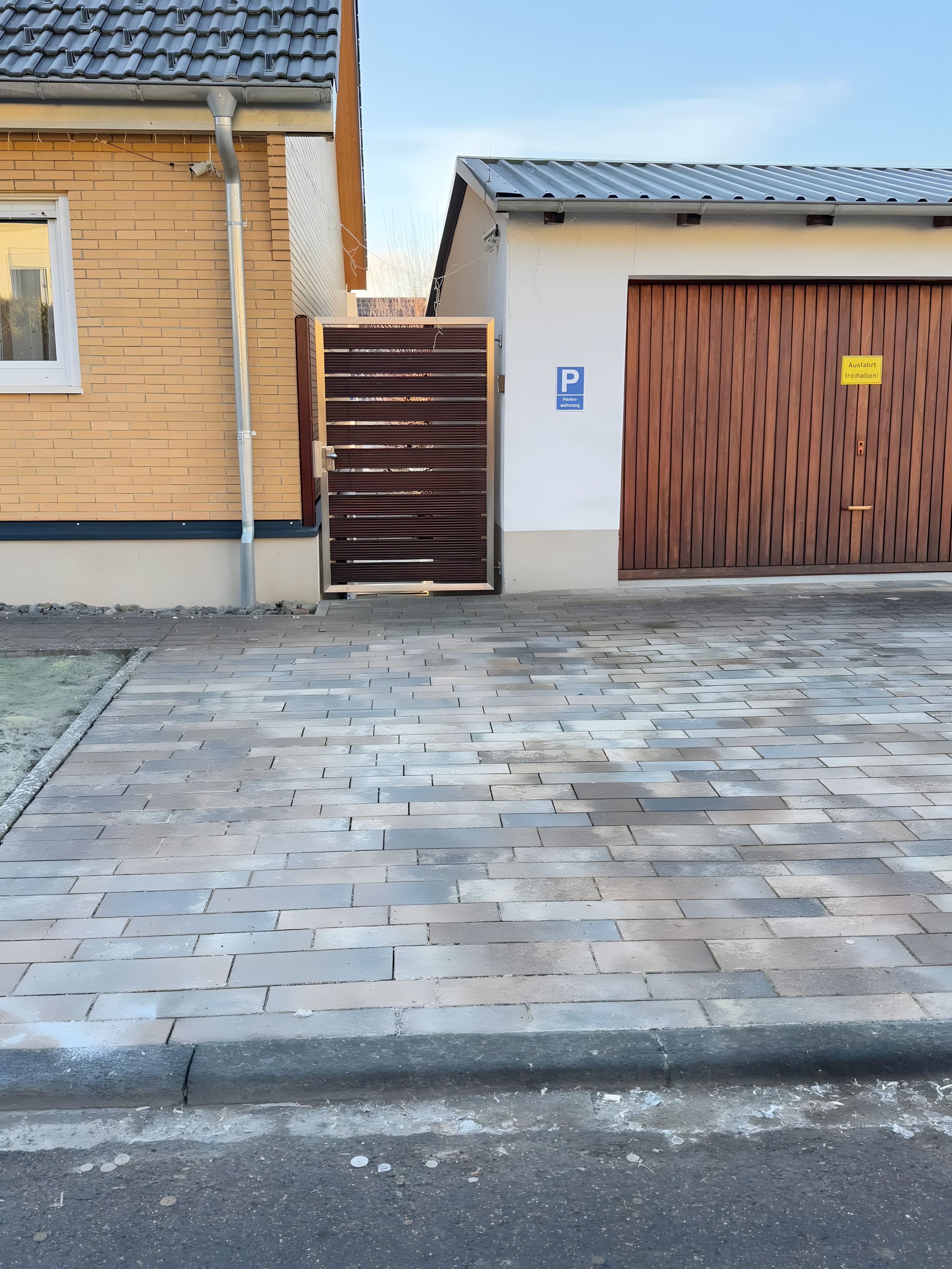 Ein verschlossenes Eingangstor mit einem Ziegelweg, der zu einem Gebäude mit einer Garagentür führt.