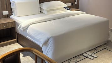 A neatly made bed with white linens, a wooden headboard, and a bedside table with a lamp. There are framed pictures on the wall above the bed.