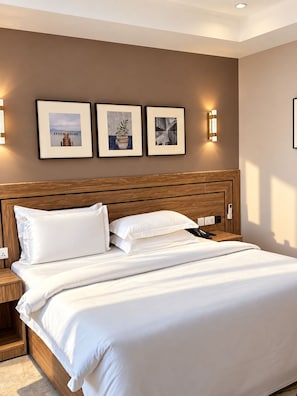 Hotellihuone, jossa on suuri sänky, puinen pääty, yöpöydät ja seinään kiinnitetyt valaisimet.
