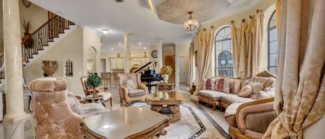 A luxurious living room with a grand piano, plush seating, and a staircase.