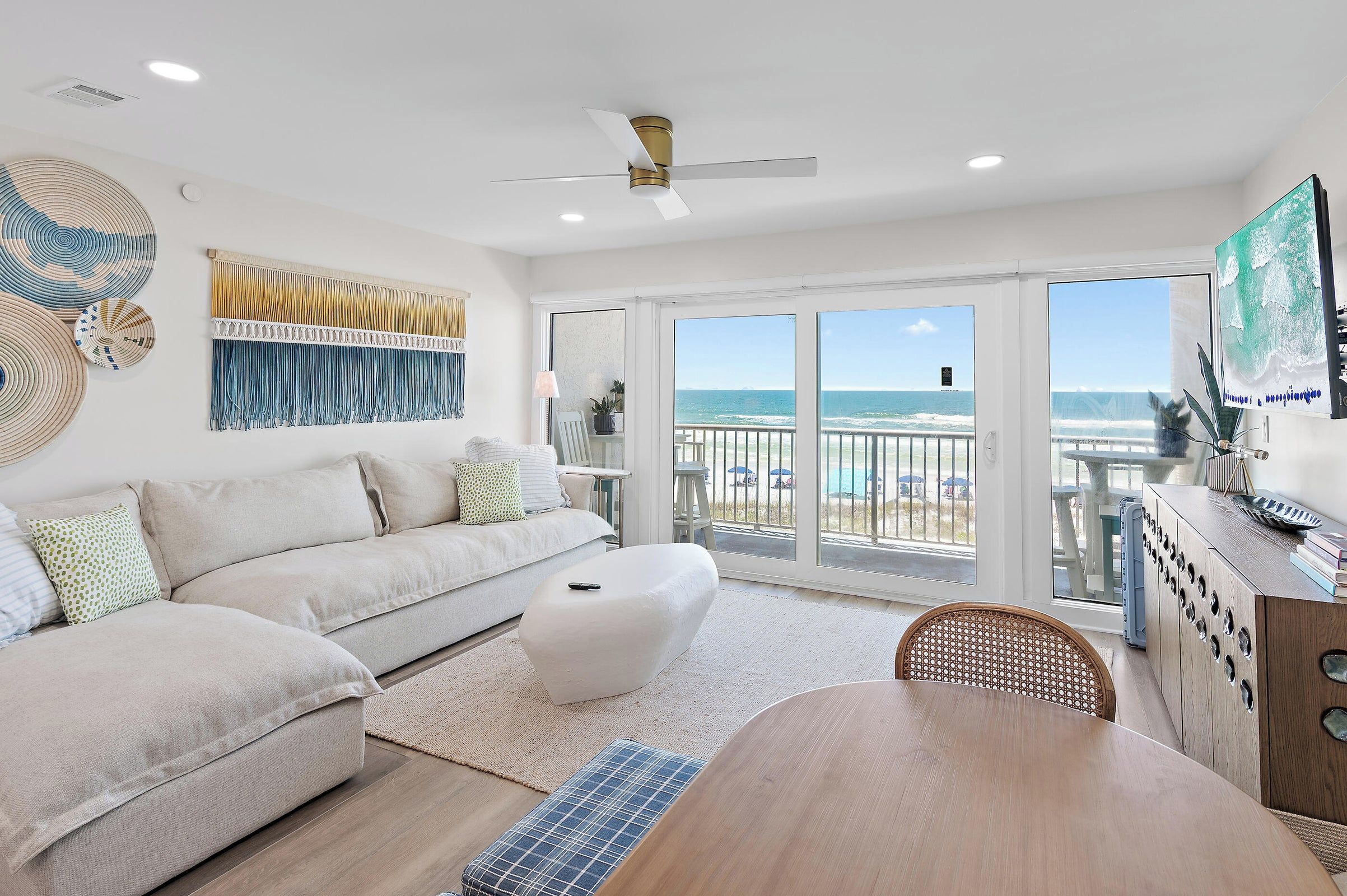 A spacious living room with a large sofa, a dining table, and a view of the beach through the sliding glass doors.