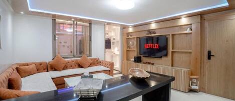 A modern living room with a sofa, a coffee table, a flat-screen TV mounted on a wooden wall, and a fireplace.