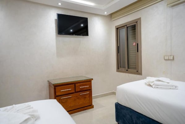 A hotel room with a bed, a wooden dresser, a television mounted on the wall, and a window with a view. - New Listing (Marrakech)