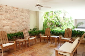 A patio area with wooden chairs and a table, surrounded by a brick wall and lush greenery. - Charming 3 Bedroom in the Old City (Cartagena de Indias)