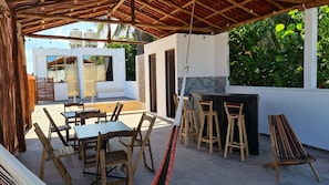 An outdoor patio with wooden furniture, a bar area, and a view of a building with a white exterior and a tiled backsplash. - New Listing (Progreso)