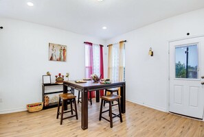 A dining area with a wooden table, four chairs, a wall-mounted shelf with decorative items, and a door with a window view. - Game Night HQ! Arcade, Pool Table & 5BR (Seguin)