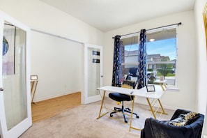 Una habitación con escritorio, silla y vistas a una zona residencial a través de una ventana.