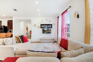 Una sala moderna con un conjunto de sofás, un televisor de pantalla plana montado en la pared y un comedor visible a través de un arco.