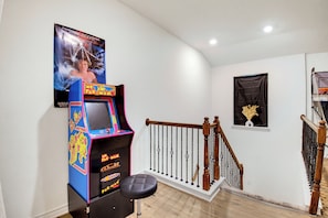 Una habitación con una máquina arcade de Pac-Man, una escalera con barandal de madera y un cartel en la pared.