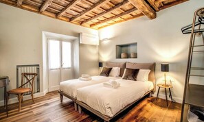 A bedroom with a wooden ceiling, a bed with white linens, a chair, a bedside table with a lamp, and a radiator. - DESIGNER ROMAN APARTMENT WITH TWO ENSUITE BEDROOMS AND A SPA-LIKE TOUCH (Roma)