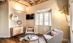 A room with a wooden ceiling, a television, a round mirror, a wooden dresser, two chairs, and a small table with a magazine. - DESIGNER ROMAN APARTMENT WITH TWO ENSUITE BEDROOMS AND A SPA-LIKE TOUCH (Roma)