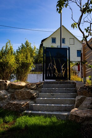 Une maison avec une entrée fermée par un portail, un escalier en pierre menant au portail, et un ciel bleu clair en arrière-plan.