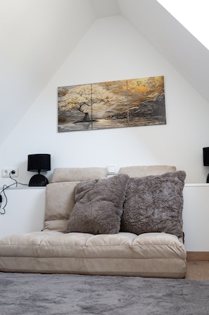 Une pièce comprenant un canapé, deux coussins, une lampe et un tableau accroché au mur.
