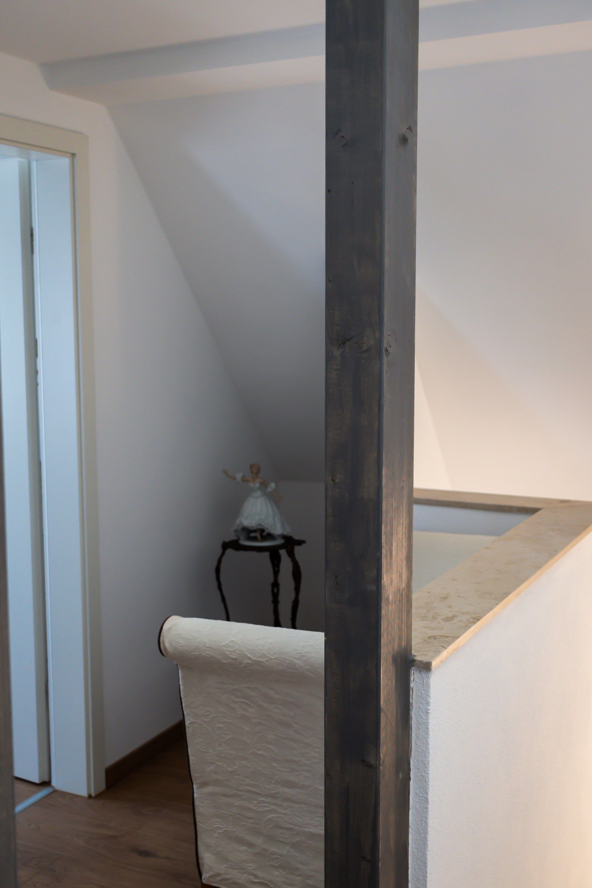 Ein Zimmer mit schrägem Dach, ein Holzstuhl mit weißem Kissen und ein kleiner Tisch mit einer Figur.
