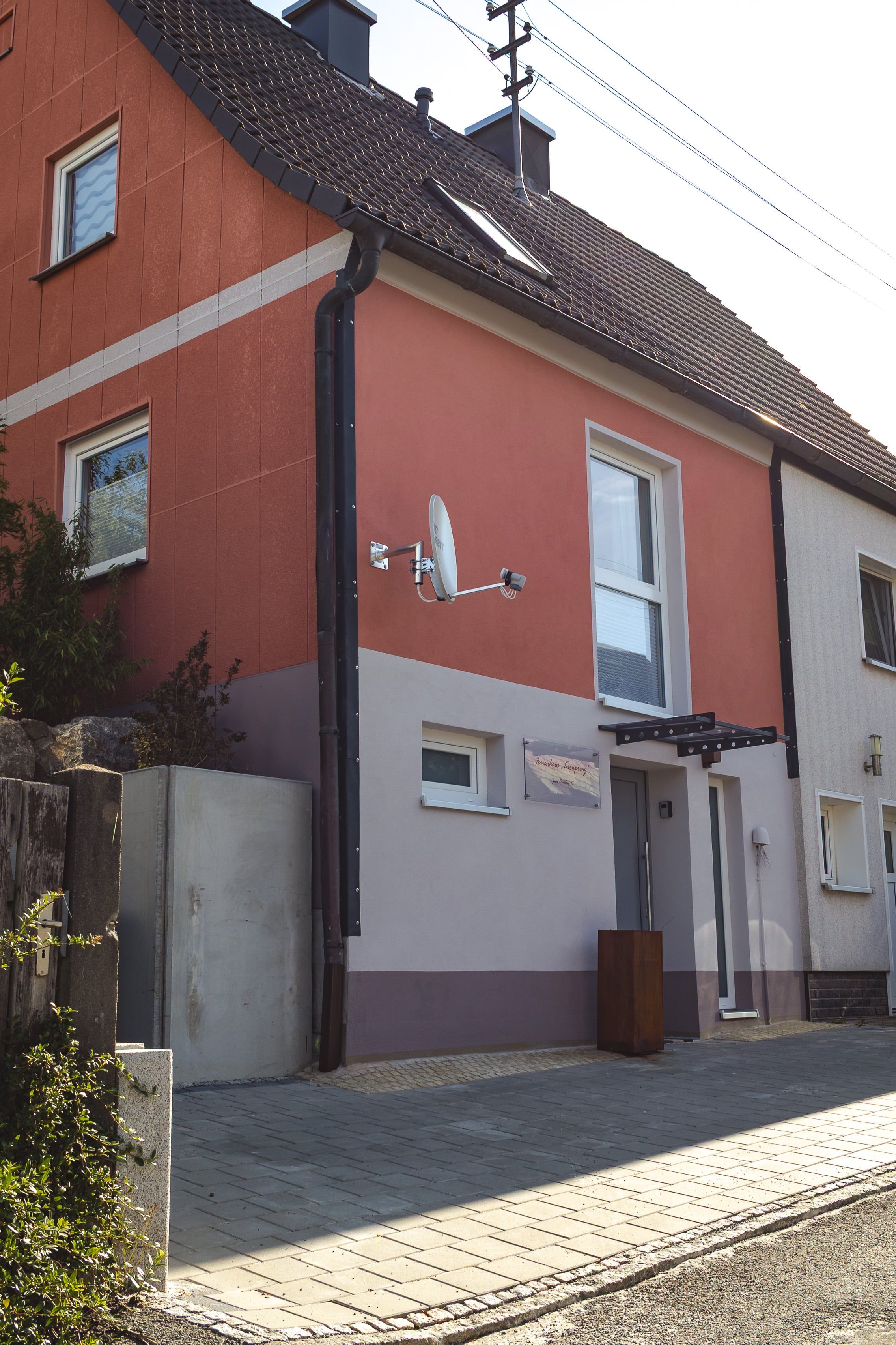 Un edificio a due piani con facciata rossa e tetto grigio. Si notano due finestre al piano terra, un ingresso e un'antenna parabolica montata sulla parete.