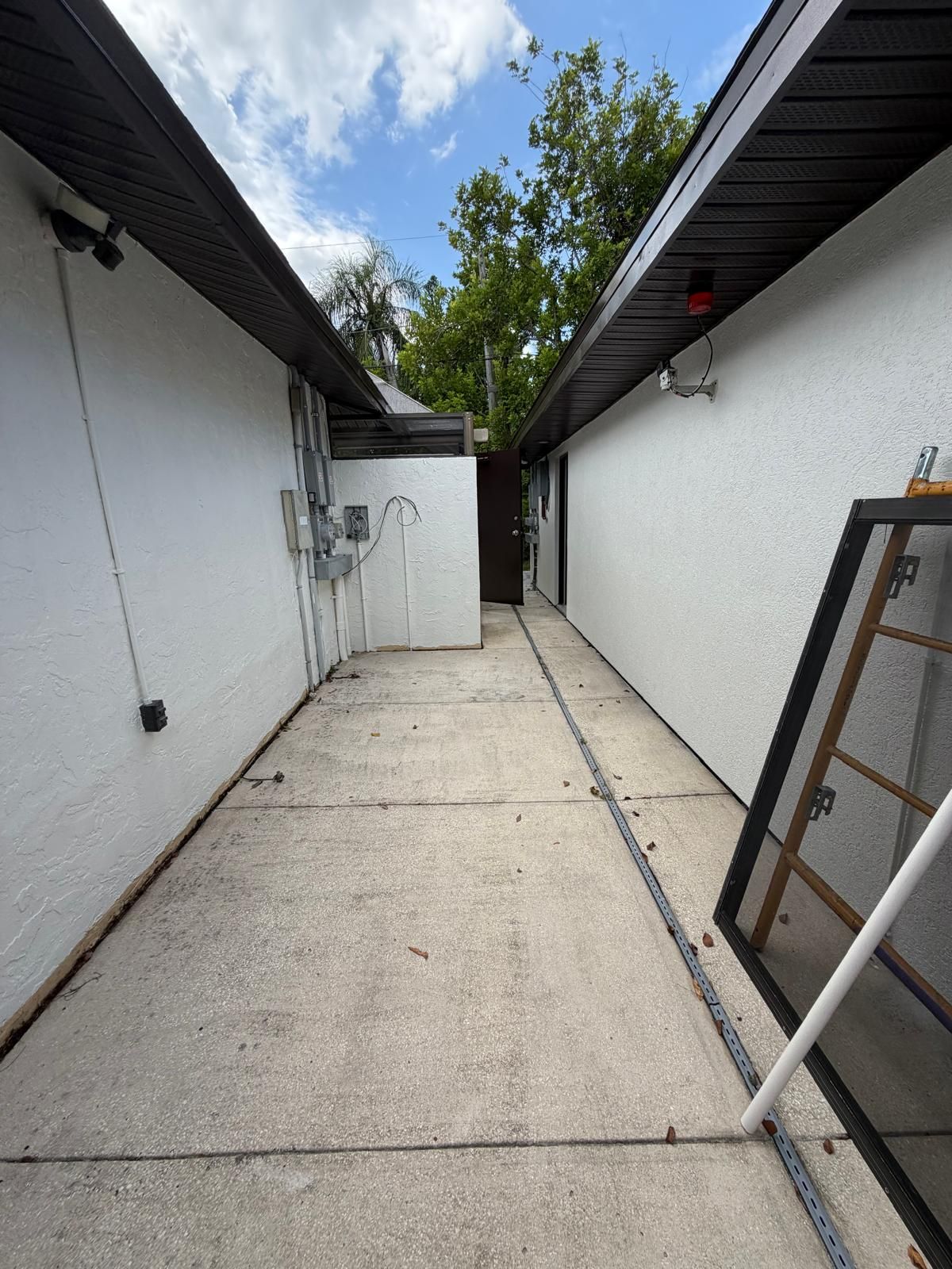 A narrow concrete pathway leading to a building entrance with a door and a window frame.