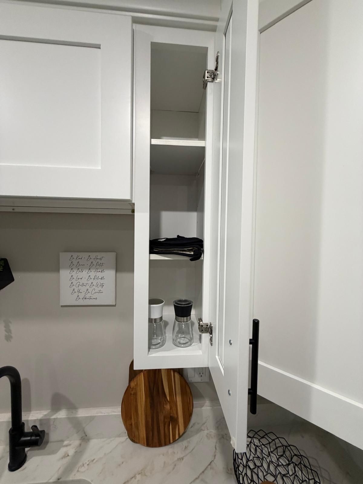 Une cuisine avec des meubles blancs, un plan de travail rond en bois, un évier et un mot écrit sur le mur.