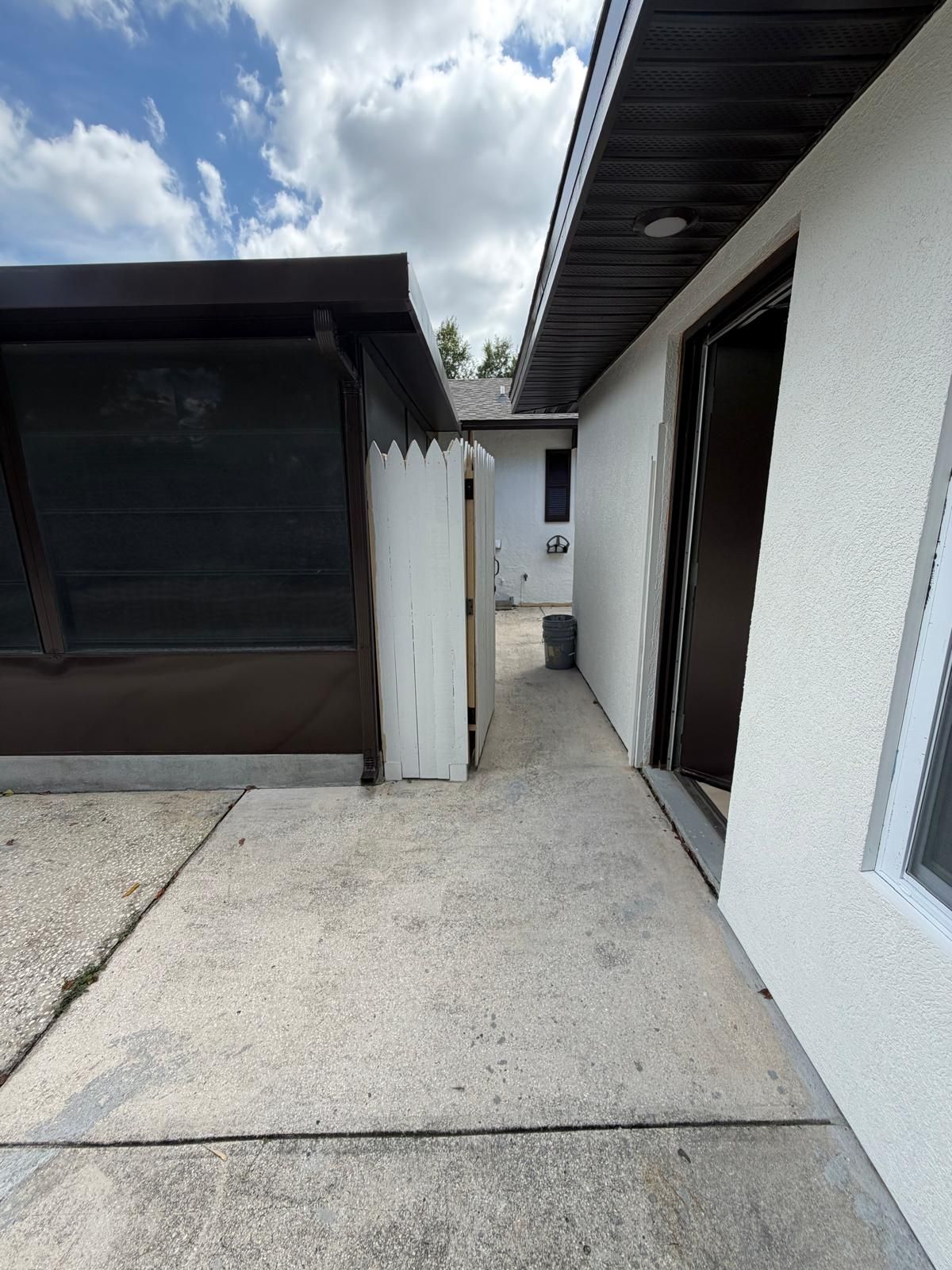 A narrow concrete pathway leading to a building with a garage door and a window.