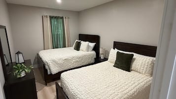 A modern bedroom with two beds, a bedside table, a mirror, and a window with curtains.