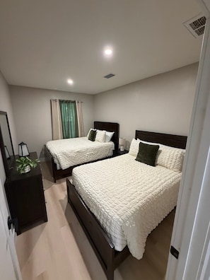 A modern bedroom with two beds, a bedside table, a mirror, and a window with curtains. - Relax & Unwind – Private Pool and Family Comfort (Pinellas Park)