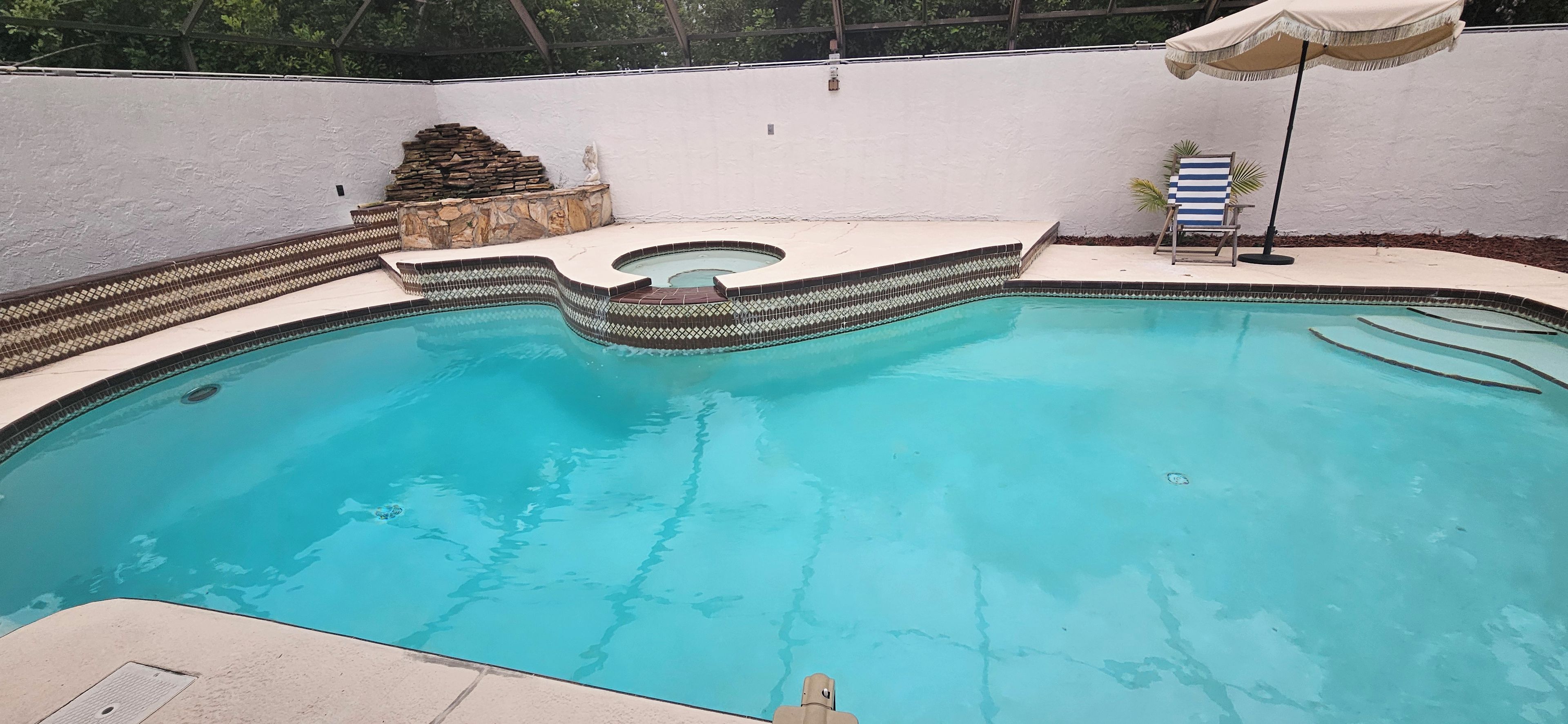A swimming pool with a curved edge, a stone feature, and a lounge chair.