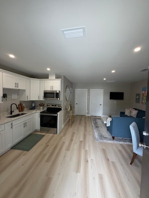 A modern kitchen with white cabinets, a microwave, and a stove. There is a dining area with a blue sofa and a TV mounted on the wall. - Relax & Unwind – Private Pool and Family Comfort (Pinellas Park)