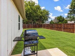 Ein Garten mit Grill, Holzzaun und Rasen.