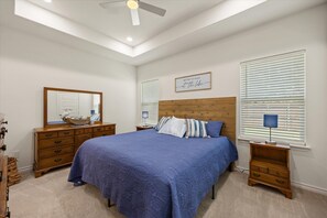 Une chambre à coucher comprenant un lit, une commode, des tables de chevet, un ventilateur de plafond et un miroir fixé au mur.