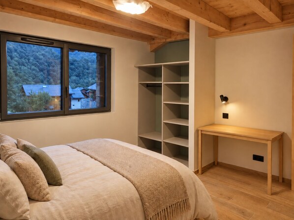 A bedroom with a bed, a window with a view of a house, a wooden desk, and built-in shelving. - New Listing (Saint-Sorlin-d'Arves)