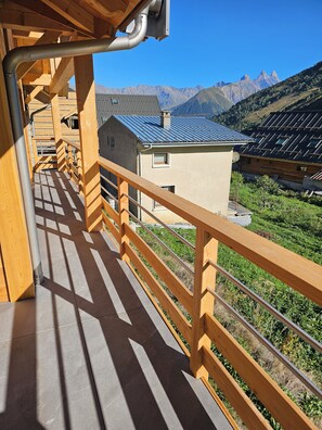 A wooden balcony with a view of a mountain range and solar panels on a building. - New Listing (Saint-Sorlin-d'Arves)