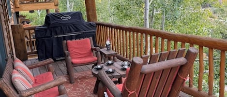 A wooden deck with outdoor furniture, a grill, and a view of trees.