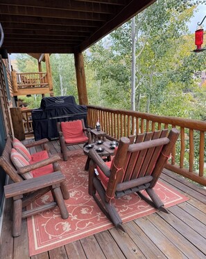 Une terrasse en bois, dotée de mobilier d’extérieur, d’un barbecue et offrant une vue sur les arbres.
