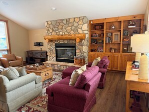 Un salon chaleureux avec une cheminée en pierre, des étagères en bois et des sièges confortables.