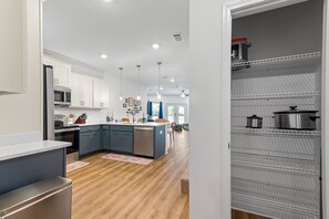 Una cucina moderna con mobili bianchi, un'isola centrale e una dispensa a tutta profondità dotata di elettrodomestici in acciaio inossidabile.