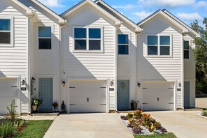 Une rangée de maisons blanches à deux étages, avec des garages attenants et des portes numérotées.