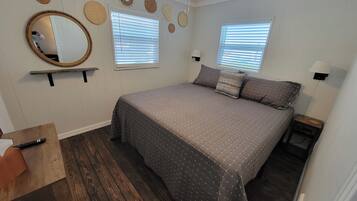 A bedroom with a large bed, two windows with blinds, a mirror, and wall decorations.
