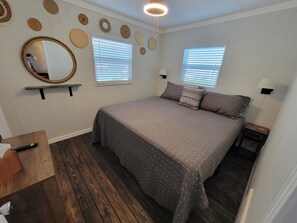 A bedroom with a large bed, two windows with blinds, a mirror, and wall decorations. - Lake Dora cabana with pool, hot tub and dock (Tavares)