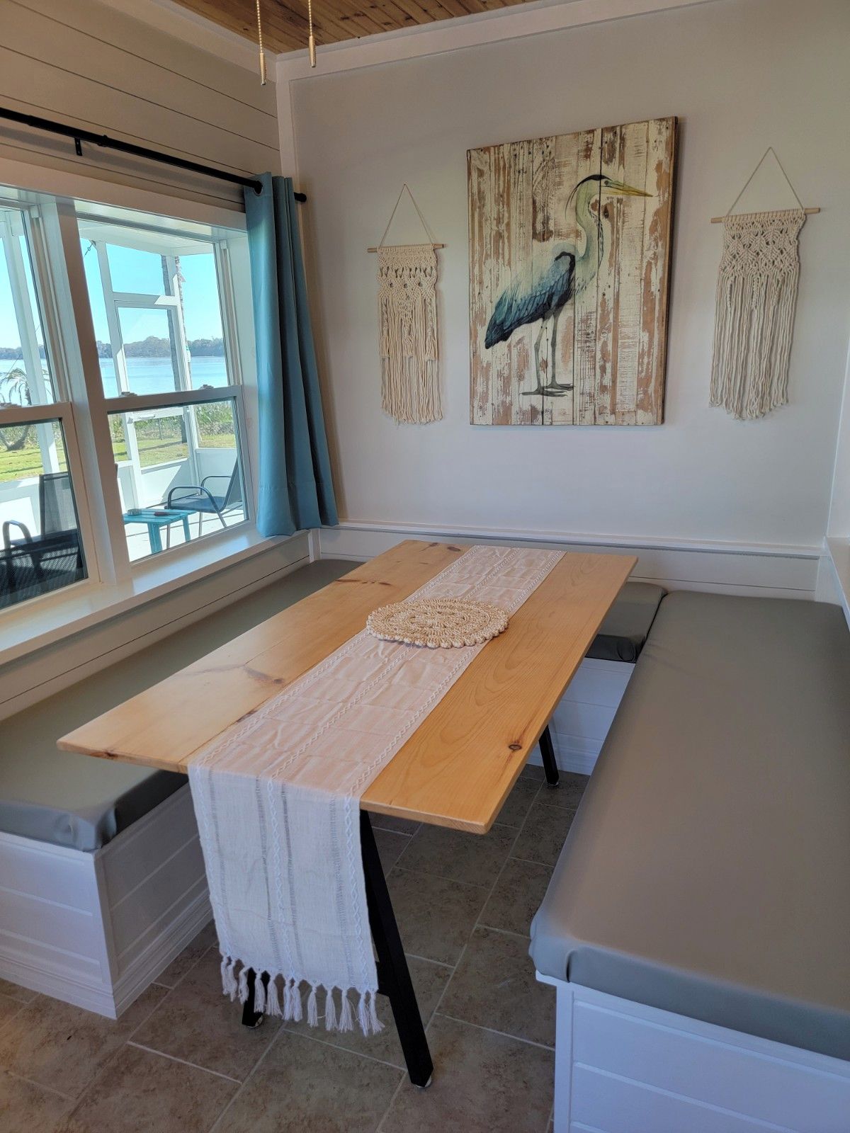 A room with a long wooden table, a bench, and a view of the outdoors through large windows.
