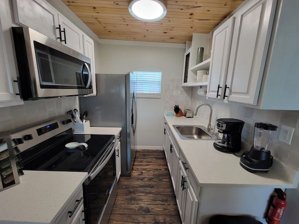 A compact kitchen with white cabinetry, a built-in microwave, a stainless steel sink, and a coffee maker. - Lake Dora cabana with pool, hot tub and dock (Tavares)